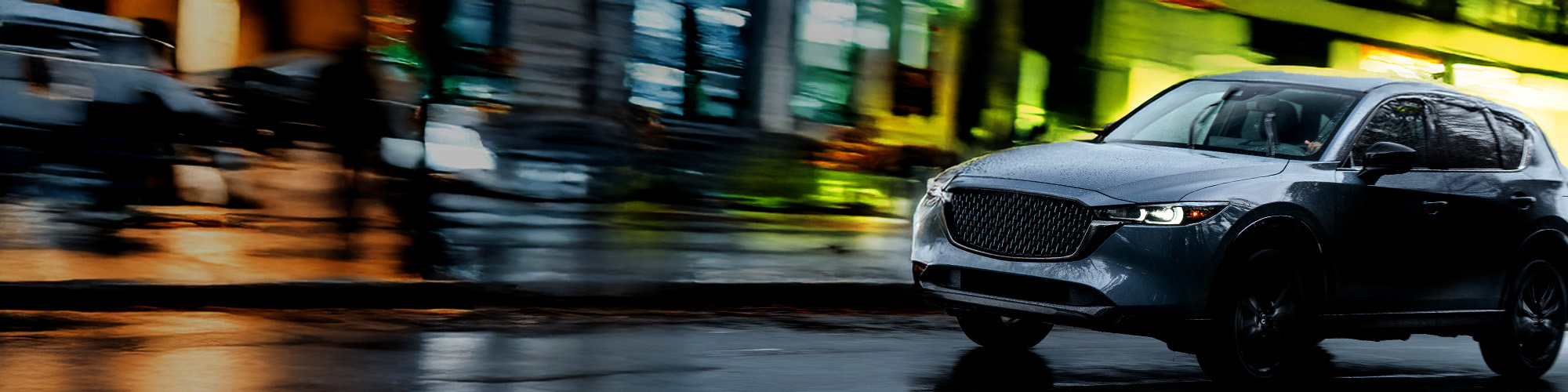 Dark gray SUV driving on wet city streets at night with reflections and motion blur, highlighting traction and urban driving performance